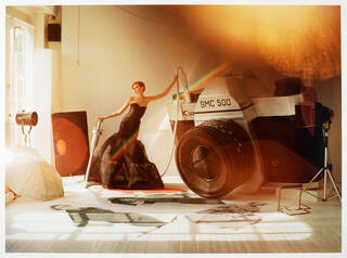 Woman stood leaning on a big camera, with the flash going off