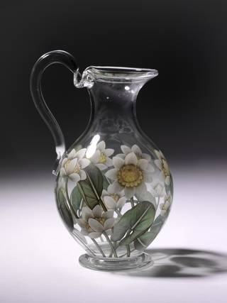 Transparent glass water jug decorated with white flowers which have a yellow centre and green stems and leaves