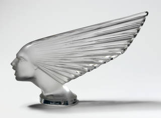 Glass radiator mascot for a car. Shaped like a screaming face, with wind blowing hair/head back in pleats