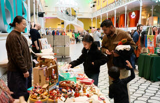 A family of 1 man and 2 children look at objects on a stall at a festive market